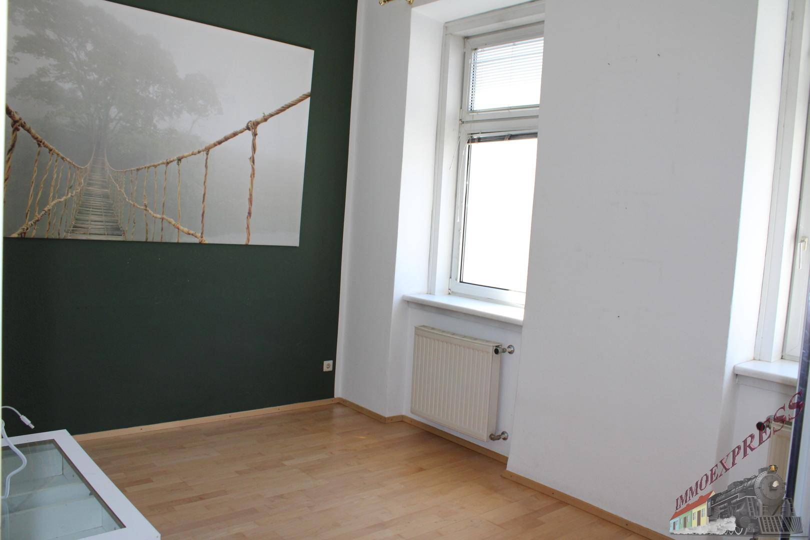 Leerer Raum mit Holzboden, weißen Wänden und einer dunkelgrünen Akzentwand mit großem Bild.