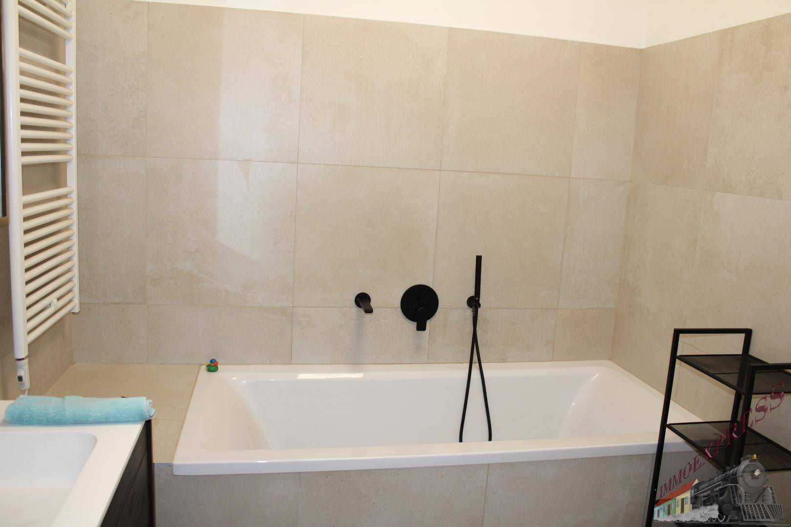 Modernes Badezimmer mit beigefarbenen Fliesen, Badewanne und schwarzer Armatur sowie Handtuchheizkörper.
