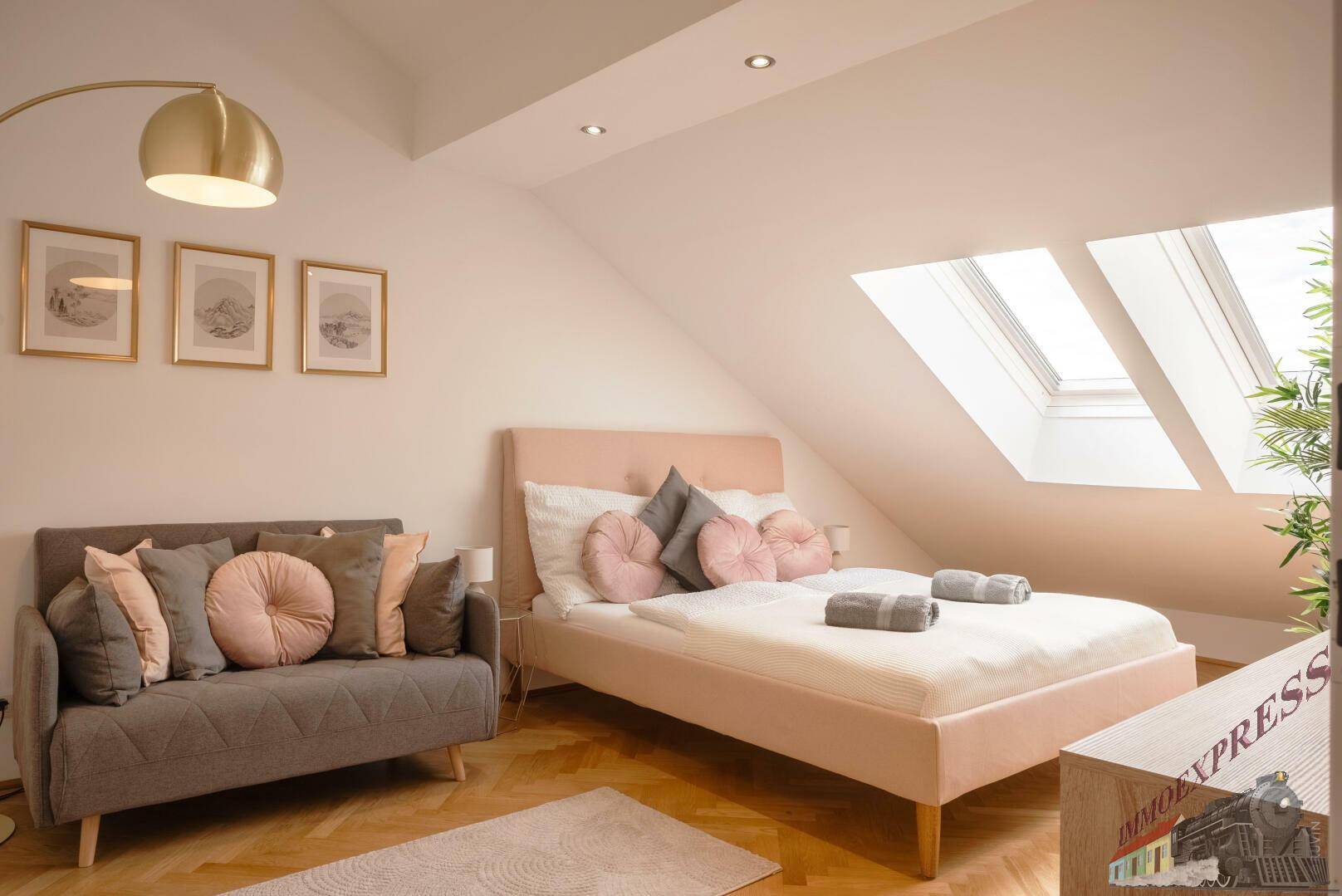 Helles Schlafzimmer mit Dachschrägen, zwei Dachfenstern und modernem Bett in Pastellfarben.