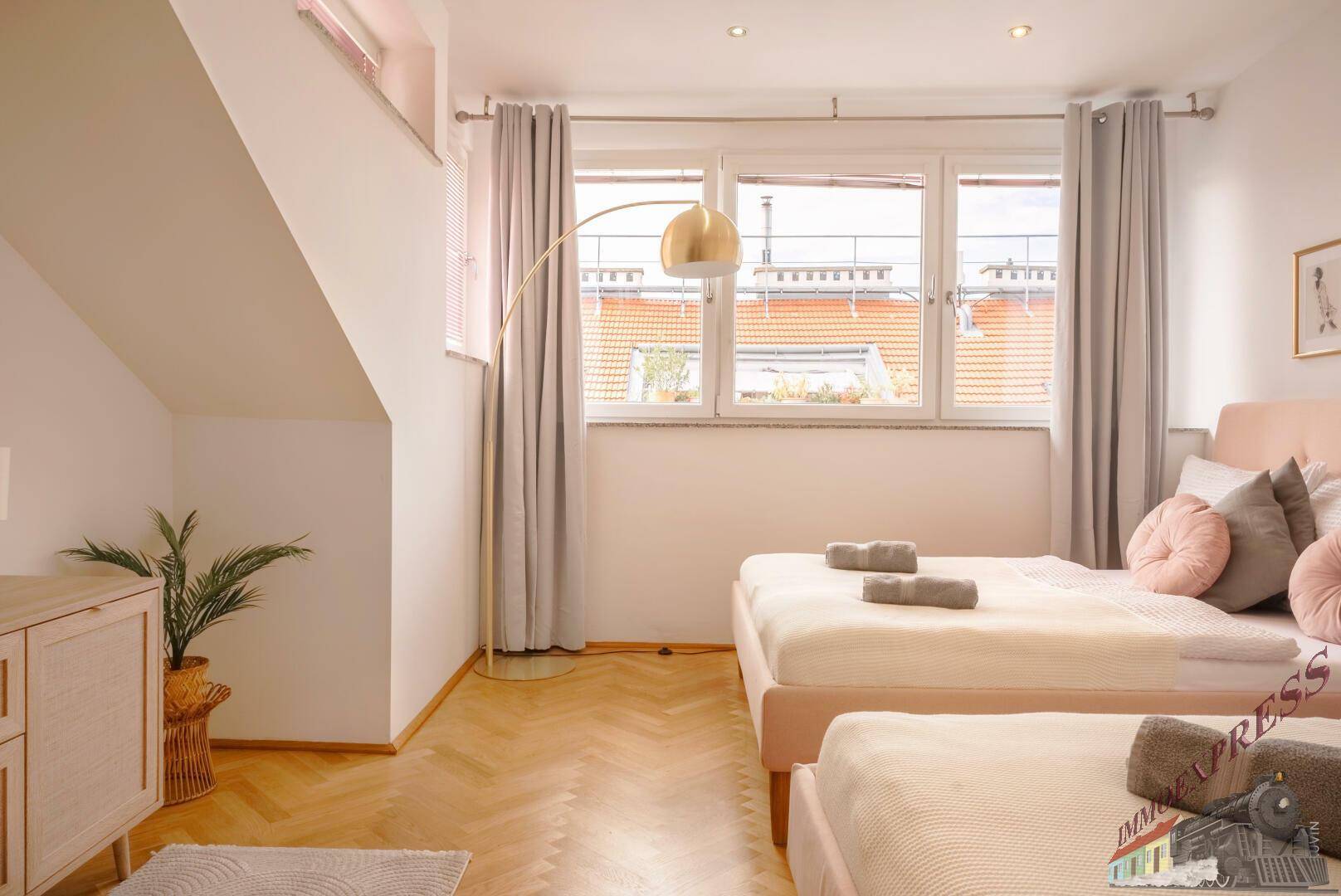 Helles Schlafzimmer mit zwei Betten, großen Fenstern und Fischgrätparkett.