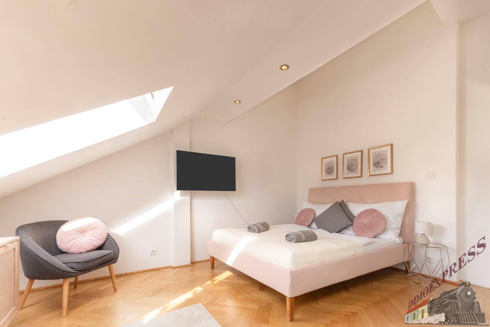 Schlafzimmer mit Dachschrägen, Dachfenster und modernem Bett sowie einem Sessel.