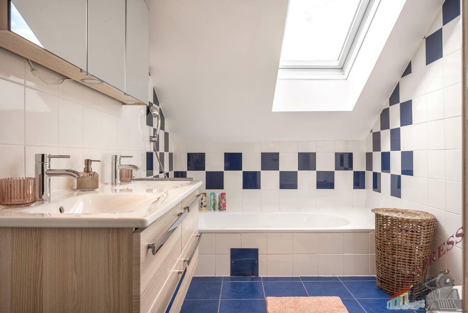 Badezimmer mit Badewanne, Dachfenster und blau-weiß karierten Fliesen unter Dachschrägen.