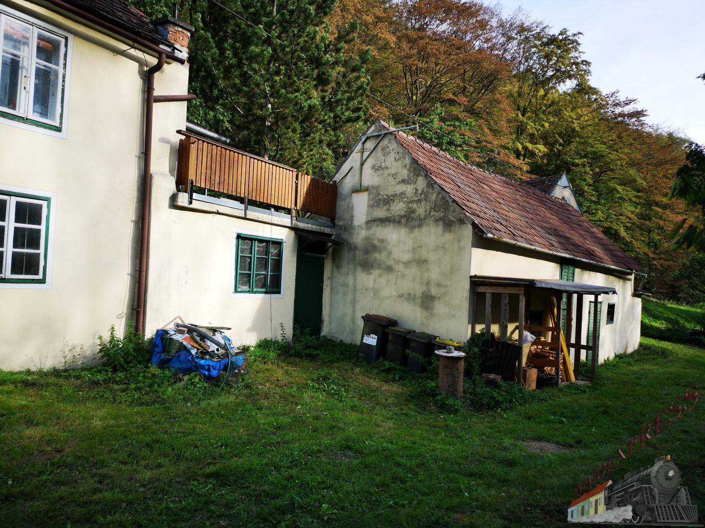 Seitenansicht des Hauses mit angrenzendem Gartenbereich und Mülltonnen, umgeben von Bäumen.