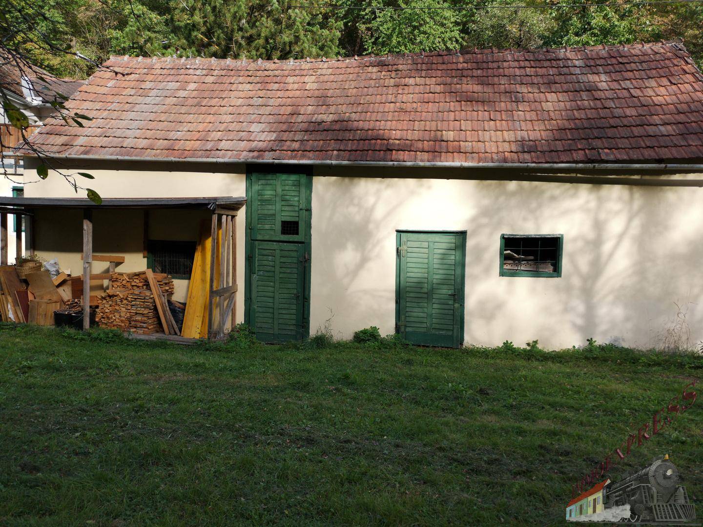 Kleines Nebengebäude mit grünen Holztüren und Ziegeldach, umgeben von einer Wiese.