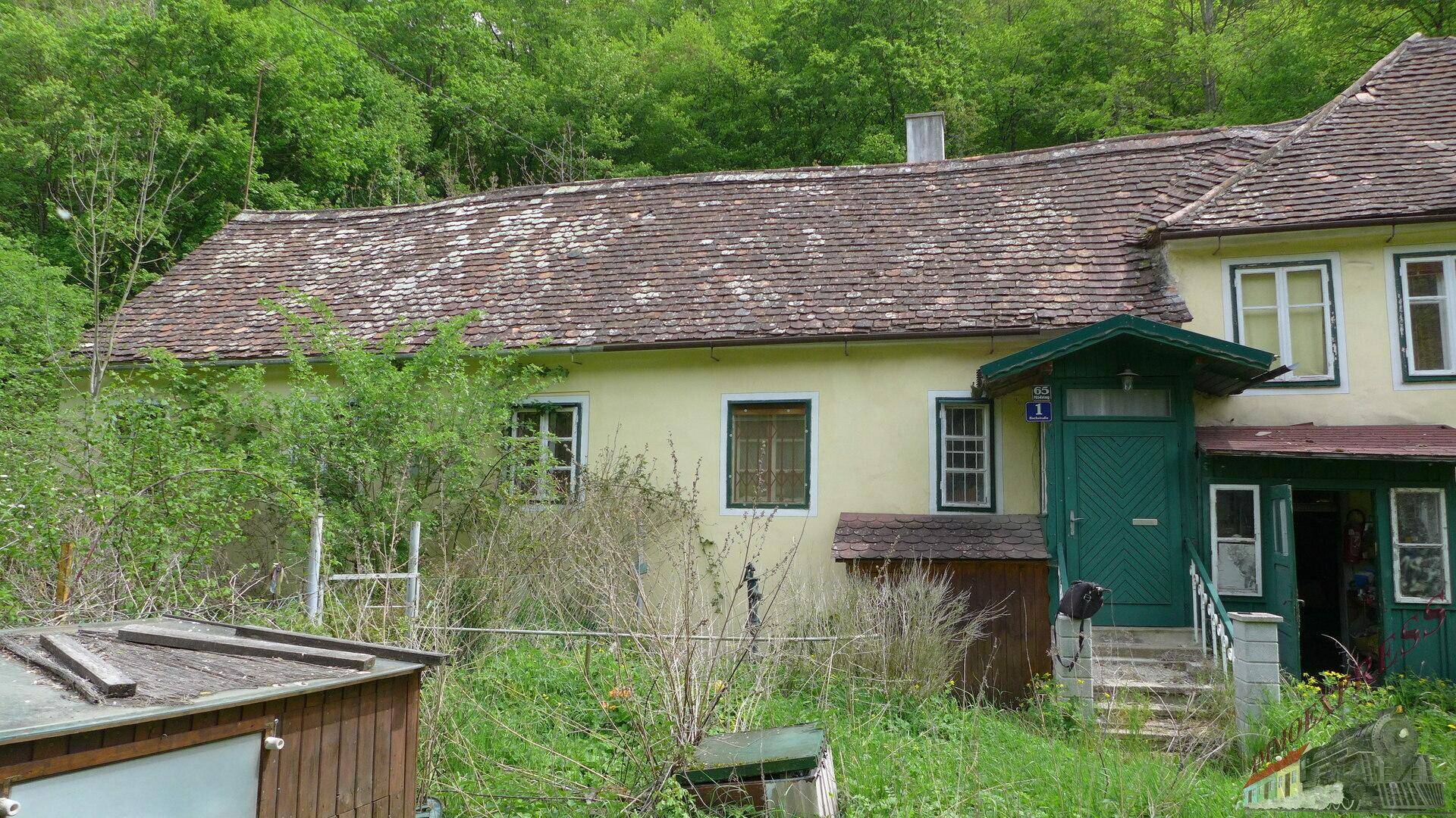 Ländliches Haus mit traditionellem Ziegeldach und grüner Eingangstür, umgeben von üppiger Natur.