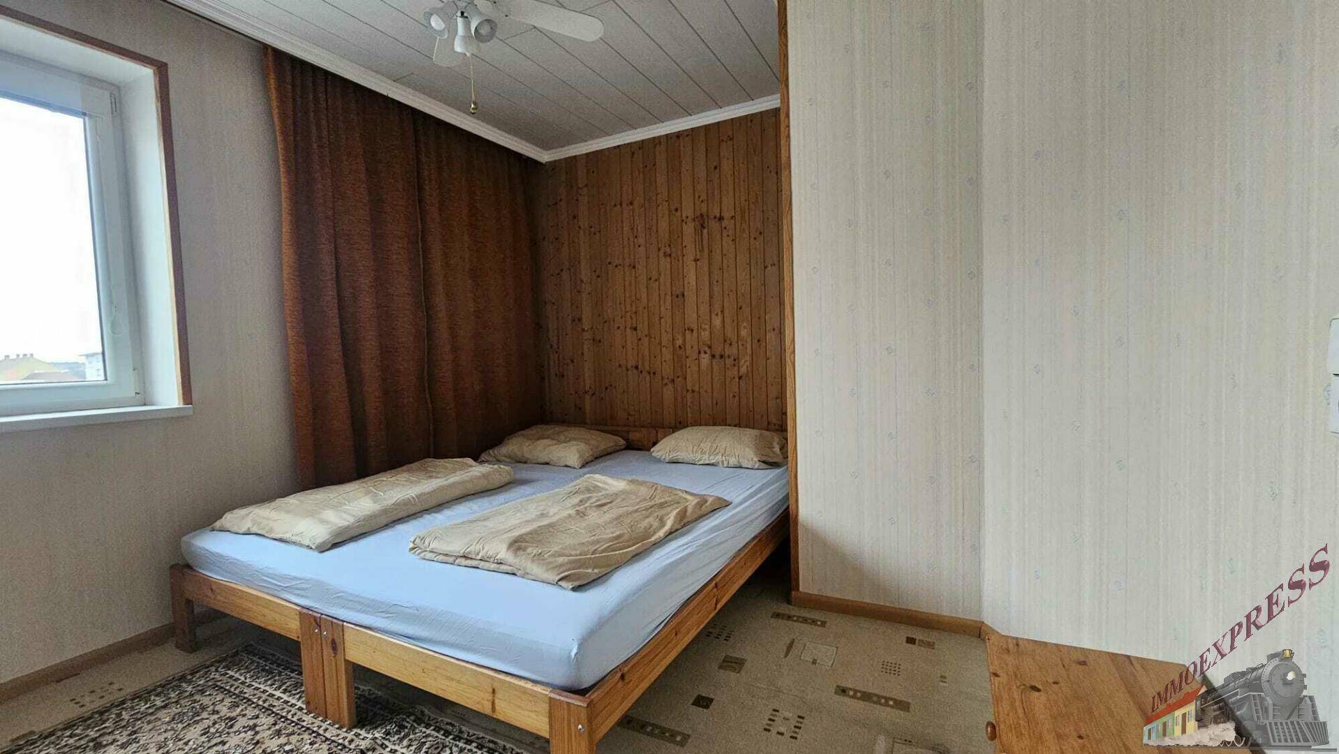 Schlafzimmer mit Doppelbett, Holzvertäfelung an der Wand und Deckenventilator für angenehme Kühlung.