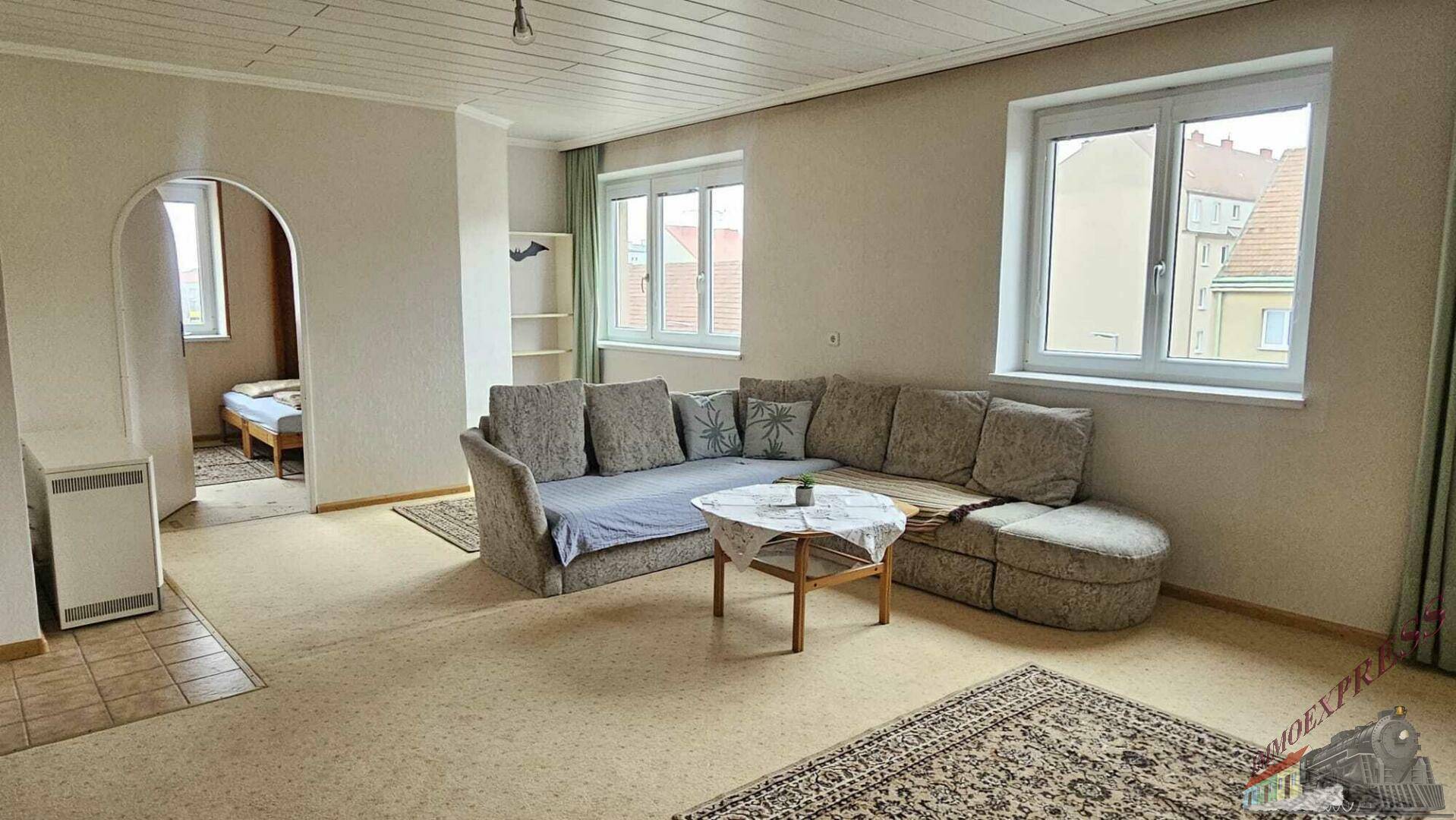 Helles Wohnzimmer mit bequemer Couch und zwei Fenstern, die viel Tageslicht hereinlassen.
