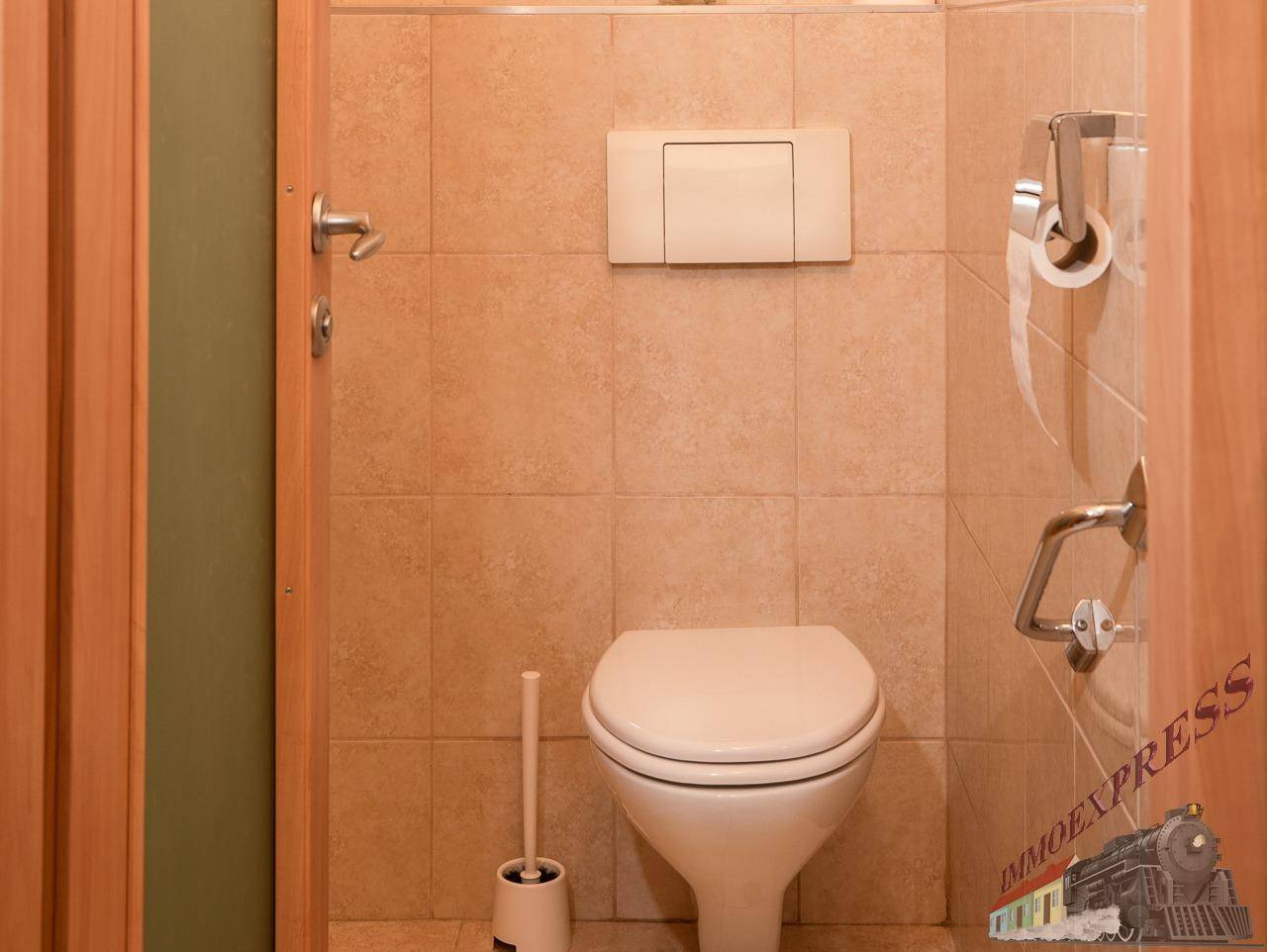 Separates WC mit Wand-WC und beigefarbenen Fliesen an Wänden und Boden.