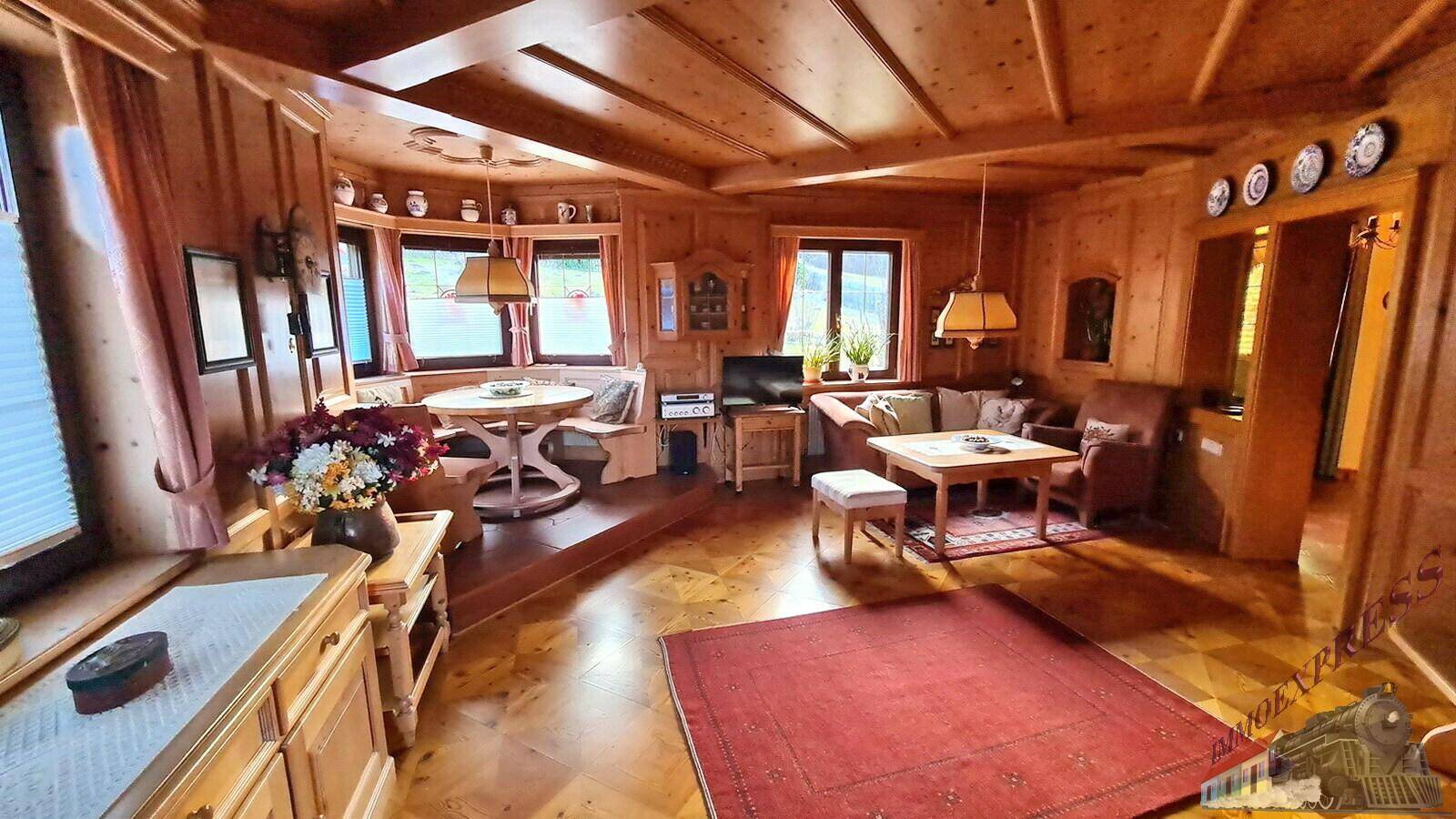 Geräumiger Wohnbereich mit Holzboden und -wänden, traditionellen Möbeln und einem gemütlichen Essbereich.