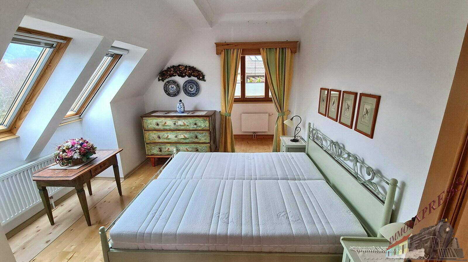 Helles Schlafzimmer im Dachgeschoss mit Holzboden, Dachfenstern und traditionellen Möbeln.