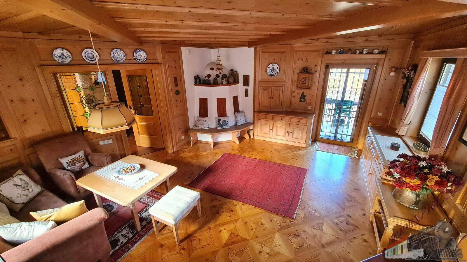 Wohnzimmer mit Holzboden und -wänden, gemütlichen Sitzgelegenheiten und einem traditionellen Kachelofen.