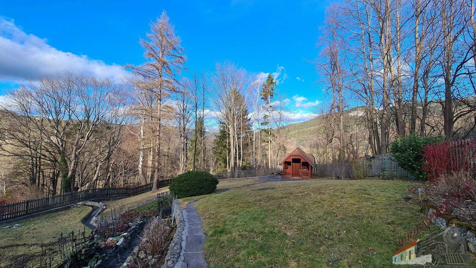 Winterlicher Garten mit einem kleinen Gartenhaus und kahlen Bäumen in der Ferne.