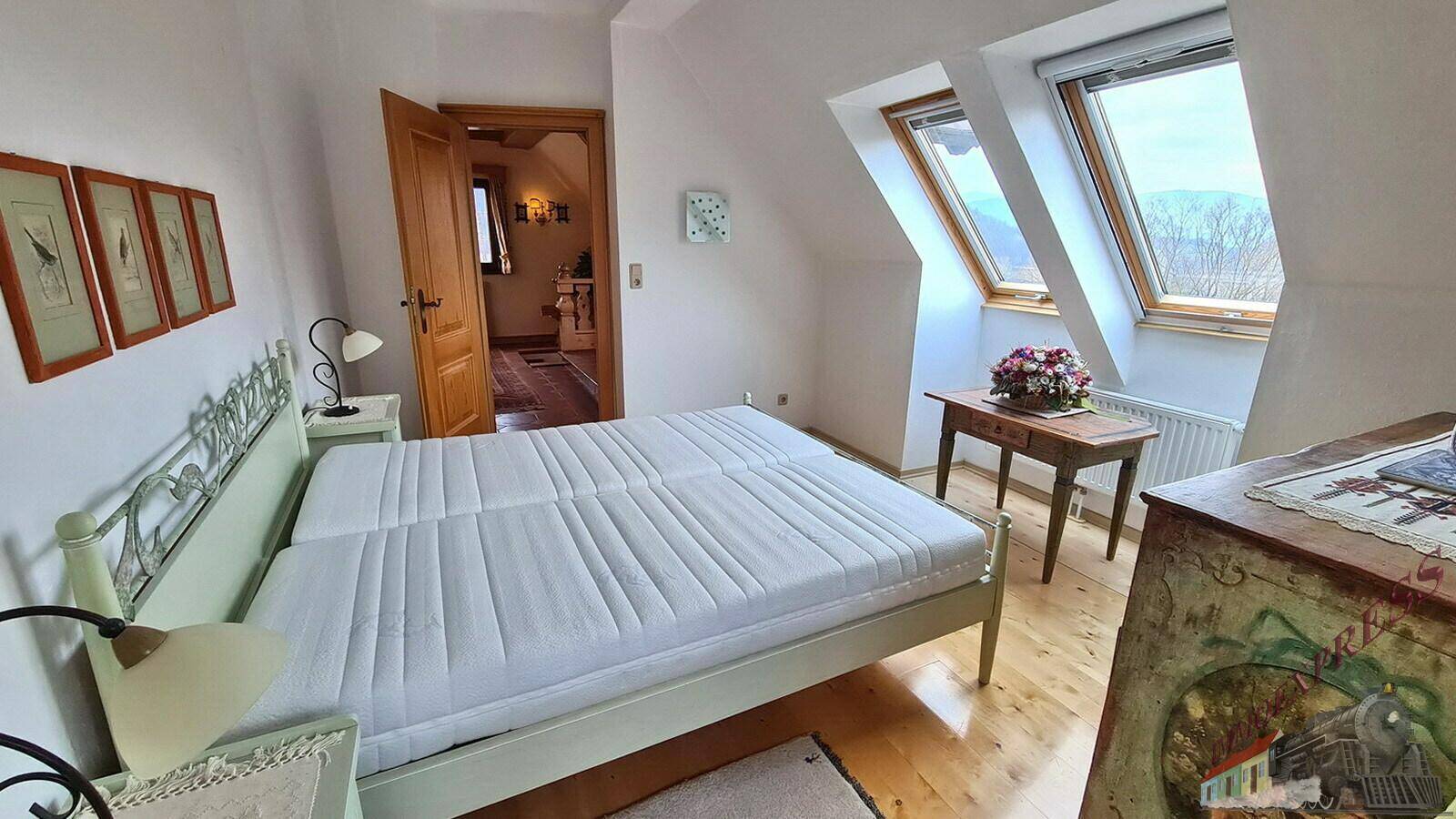 Schlafzimmer mit Holzboden und schrägen Wänden, bietet viel Tageslicht durch die Dachfenster.