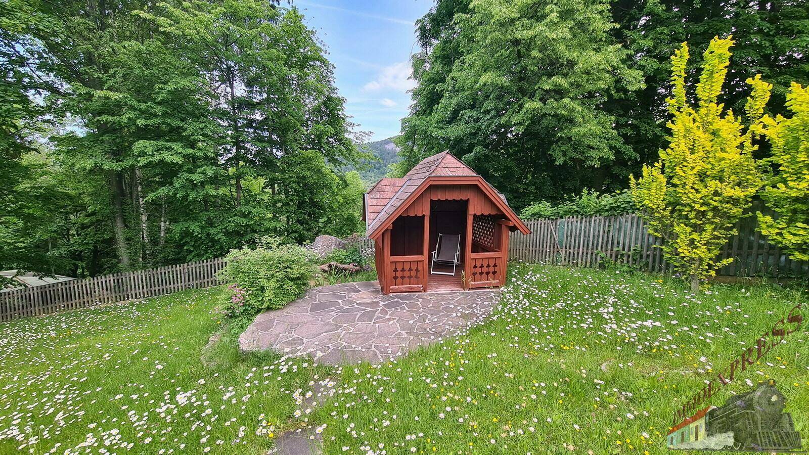 Charmantes Gartenhaus mit gepflastertem Bereich, umgeben von einer blühenden Wiese.