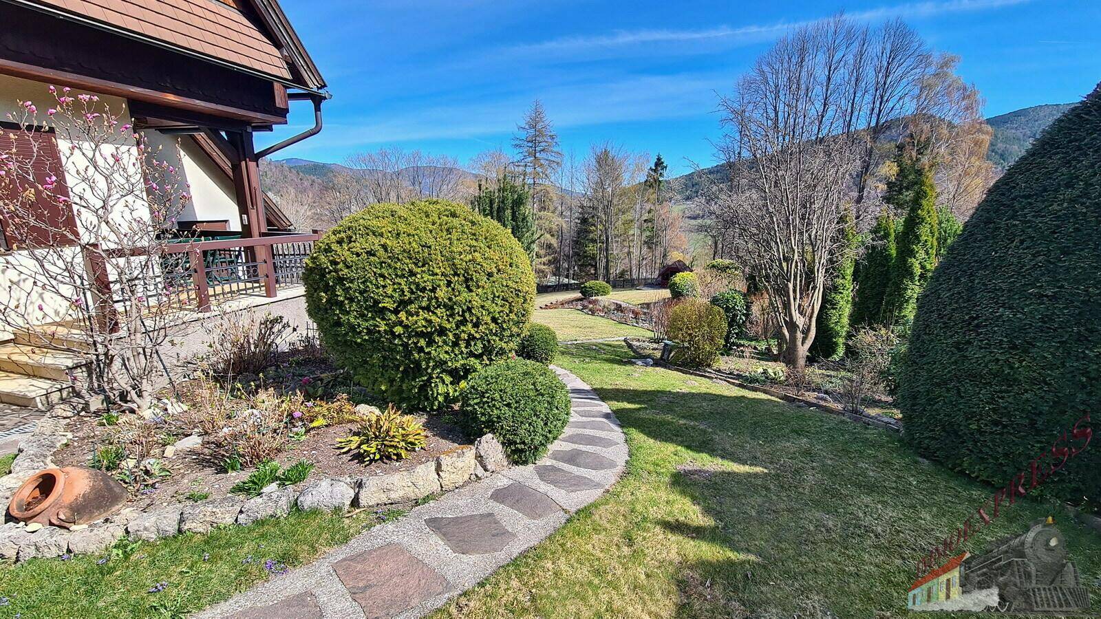 Geschwungener Steinweg führt durch den gepflegten Garten mit Sträuchern und Blumenbeeten.