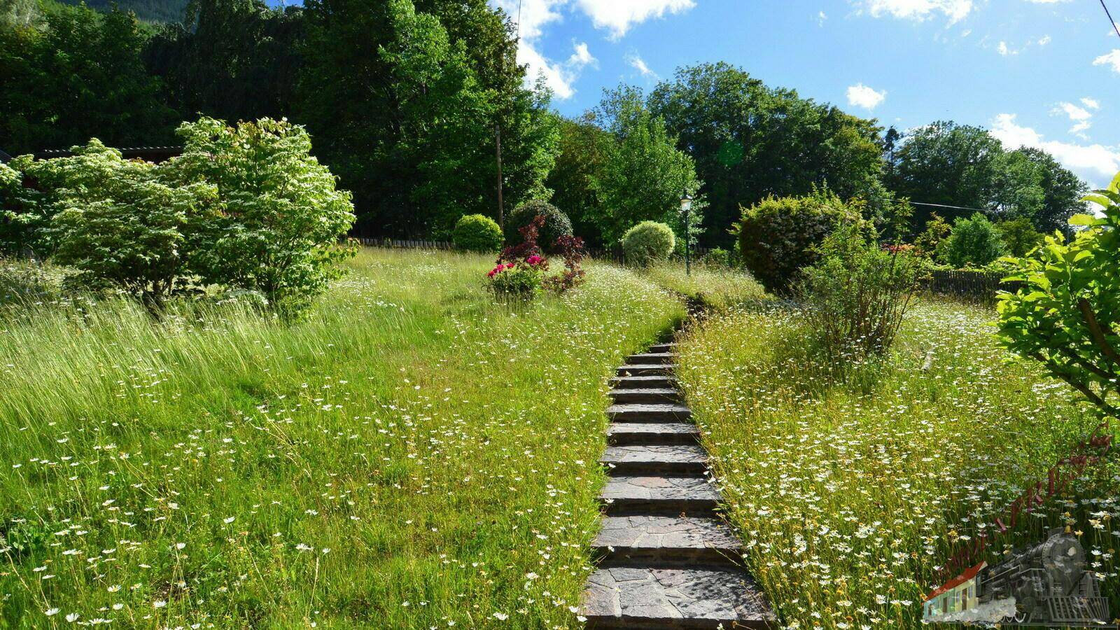 Steinweg mit Stufen führt durch die blühende Wiese des weitläufigen Gartens.