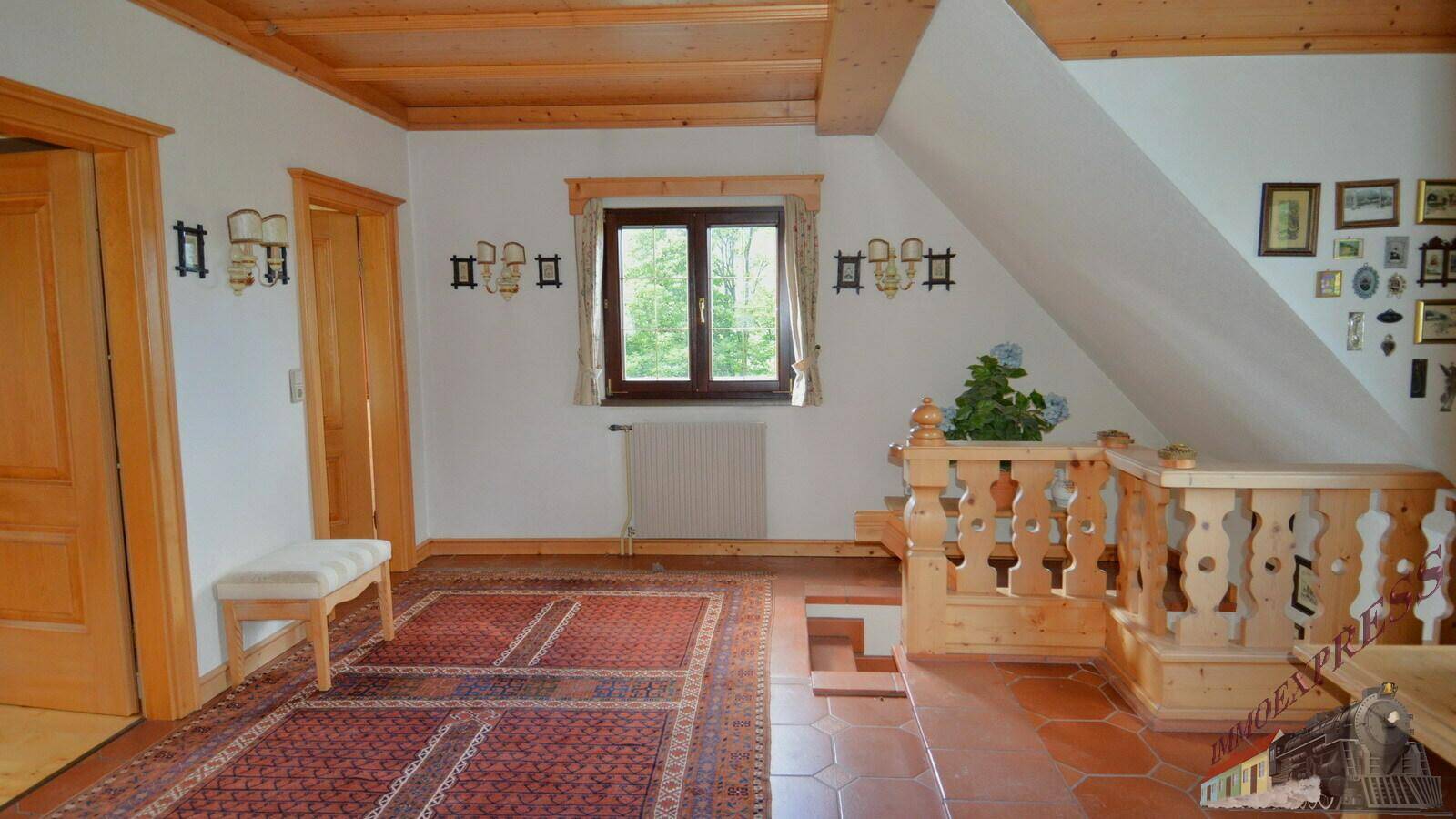 Heller Flur im Obergeschoss mit Holzboden und -decke, traditionellem Geländer und Blick ins Grüne.