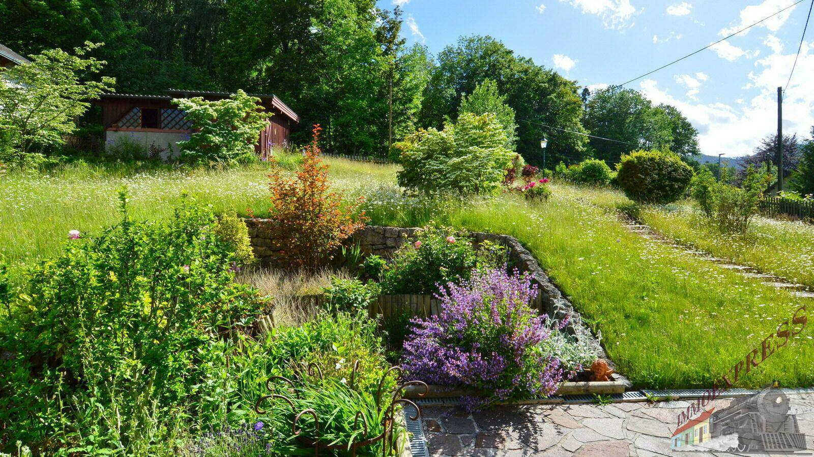 Terrassierter Gartenbereich mit verschiedenen Pflanzen und einem kleinen Gartenhaus im Hintergrund.