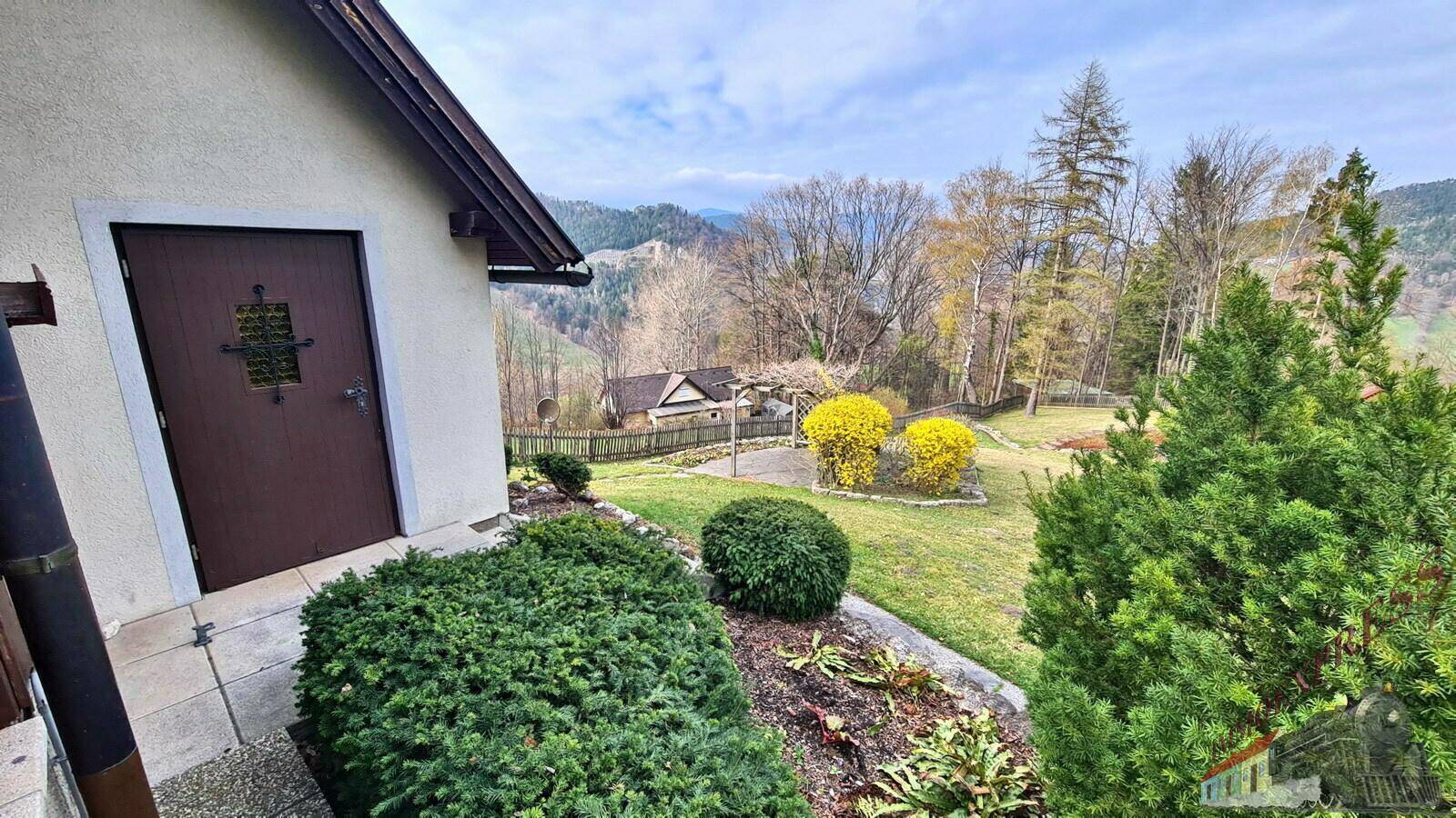 Seitenansicht des Hauses mit Eingangstür und Blick auf den weitläufigen Garten.