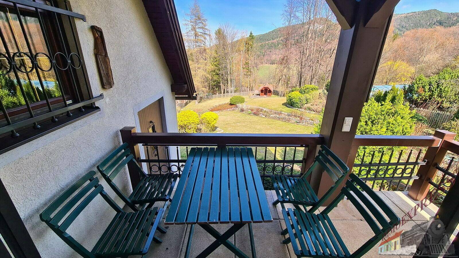 Balkon mit Sitzgelegenheiten und weitem Blick auf die umliegende Berglandschaft und das grüne Tal.