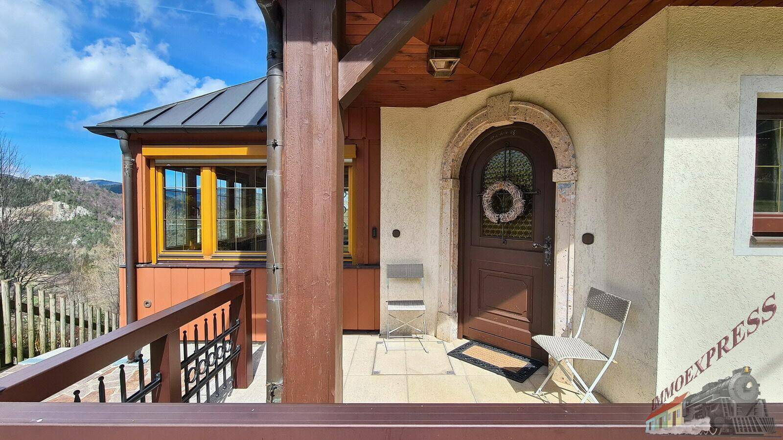 Eingangsbereich des Hauses mit Holztür und kleiner Veranda, umgeben von traditionellen Elementen.