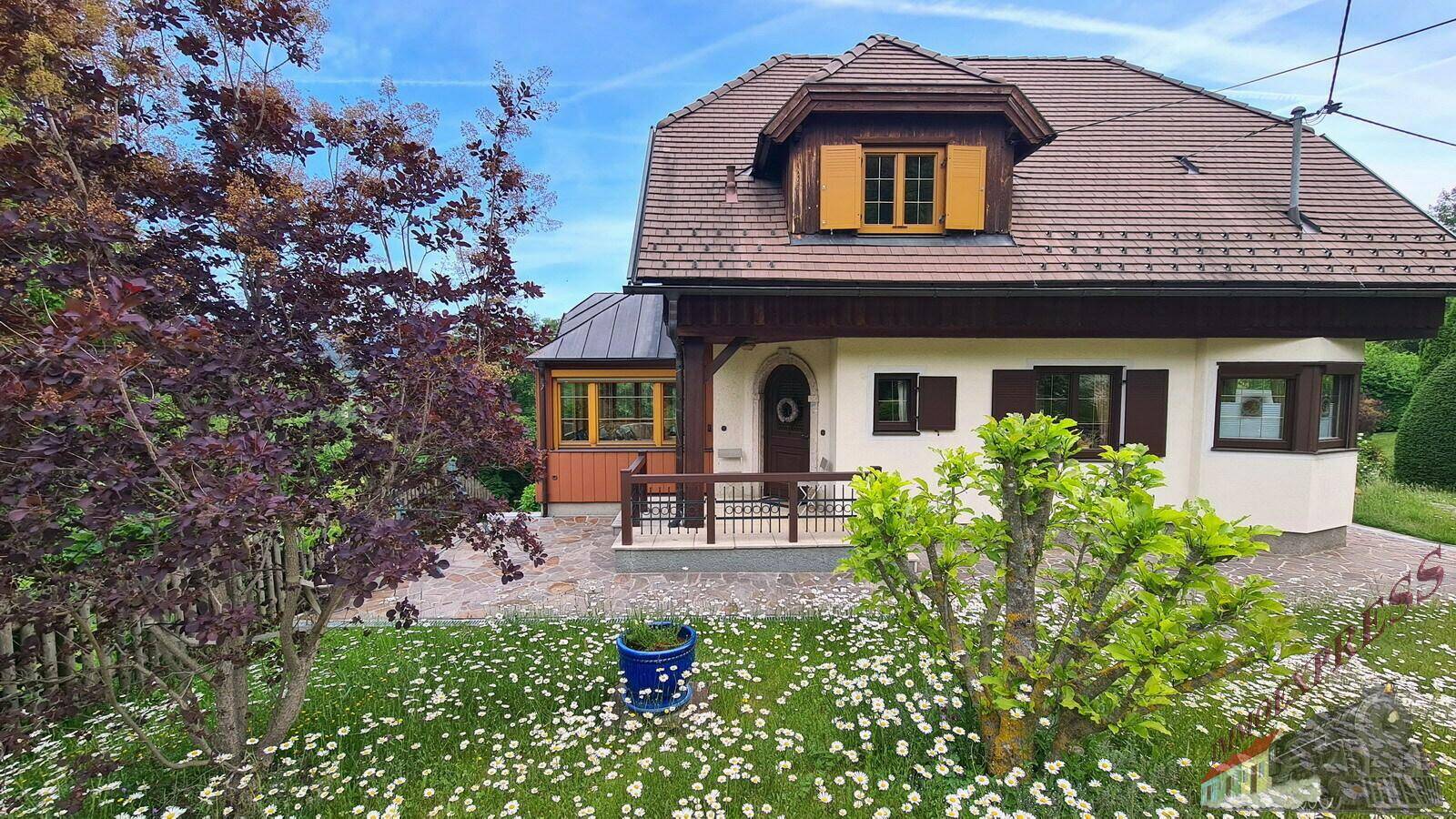 Charmantes Einfamilienhaus mit traditioneller Architektur, umgeben von einem blühenden Garten und grüner Landschaft.