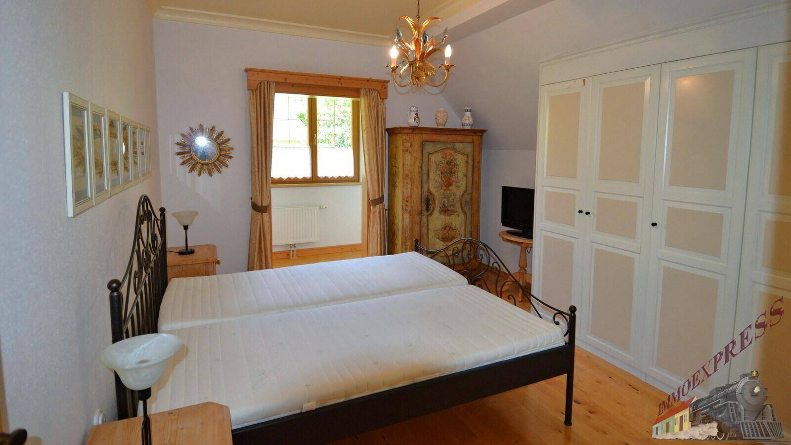 Helles Schlafzimmer mit Holzboden, Einbauschränken und einem Fenster mit Blick ins Grüne.