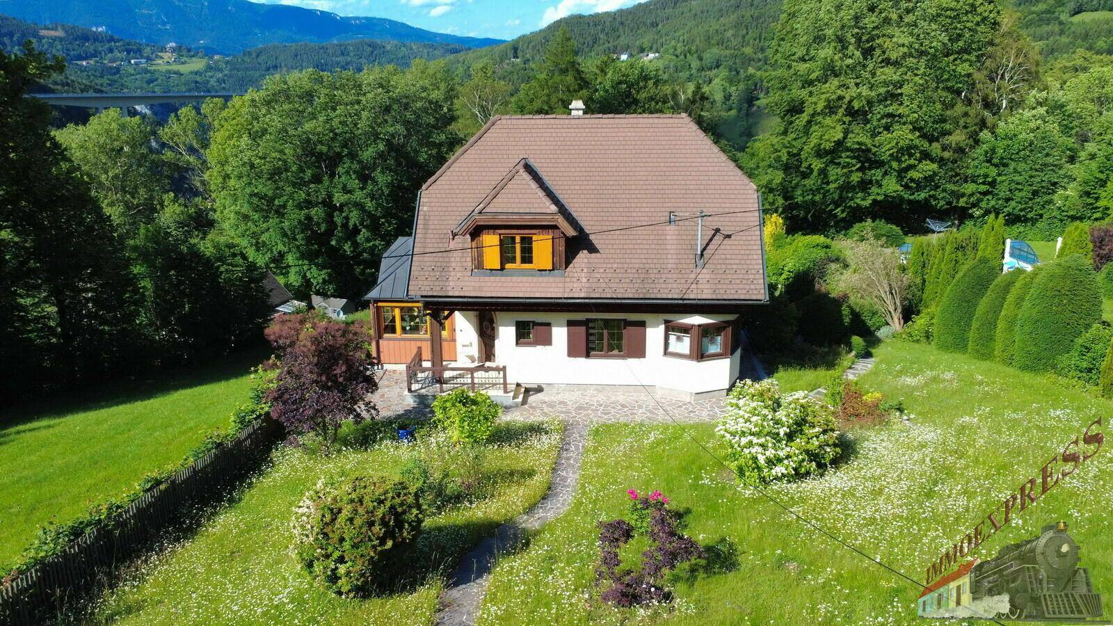 Luftaufnahme des Hauses mit weitläufigem Garten und Blick auf die umliegende Berglandschaft.