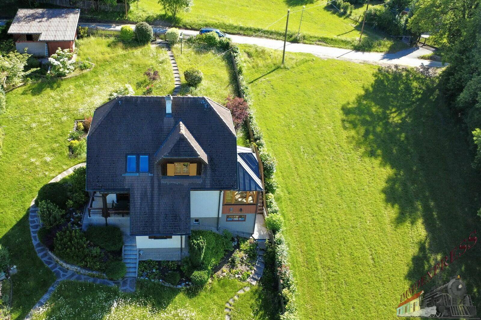 Luftaufnahme des Hauses von der Rückseite mit Mansarddach und angrenzendem Hanggrundstück.