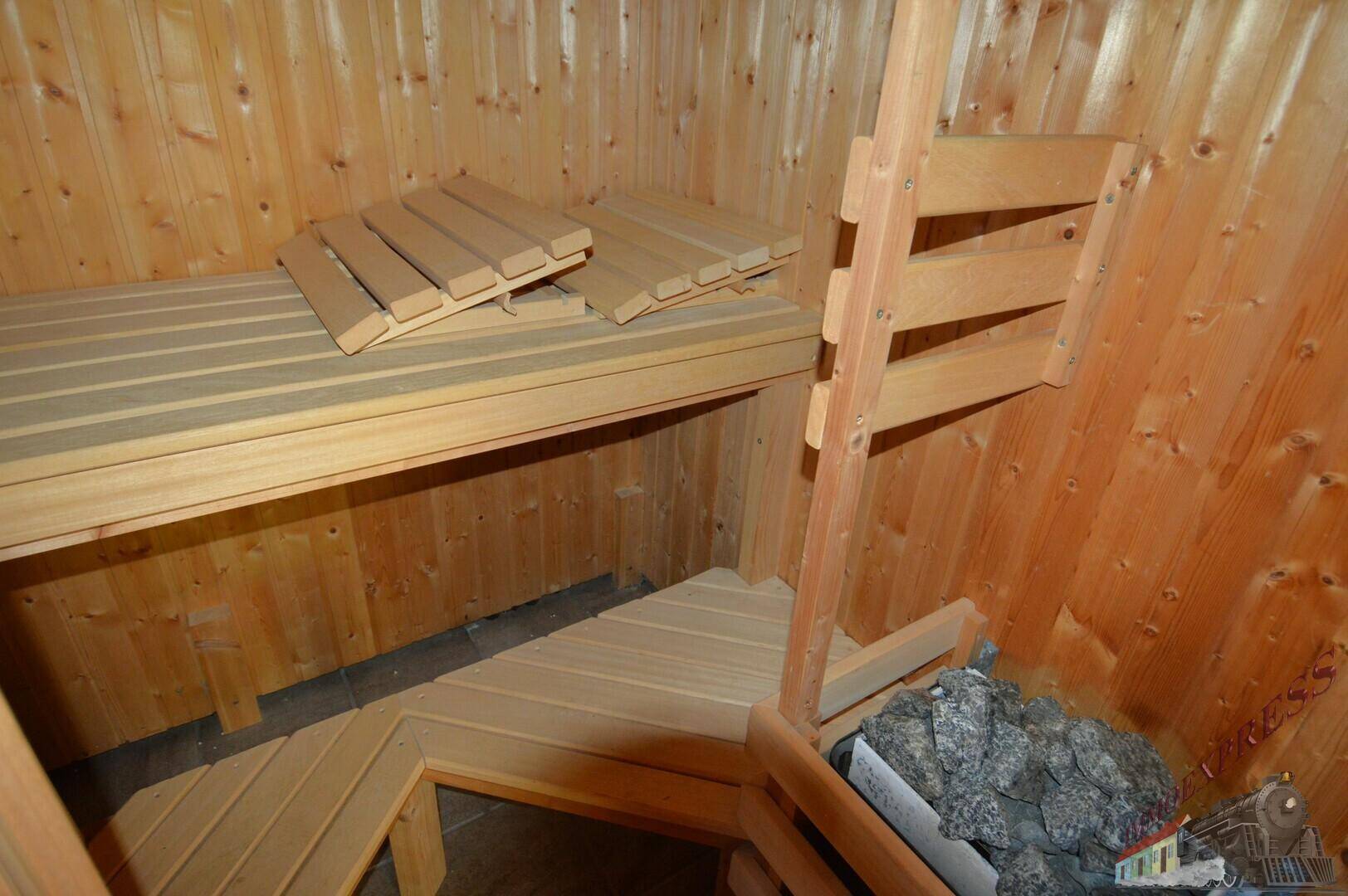 Innenansicht einer Holzsauna mit Sitzbänken und Saunaofen mit Steinen.