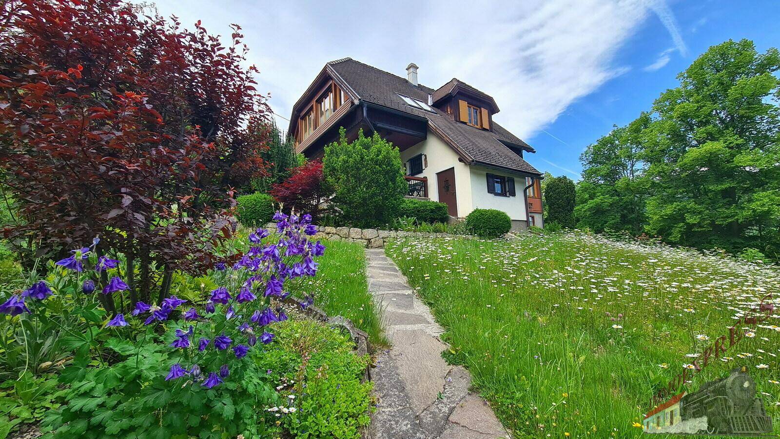 Blühender Gartenweg mit lila Blumen führt zum idyllischen Haus in ländlicher Umgebung.
