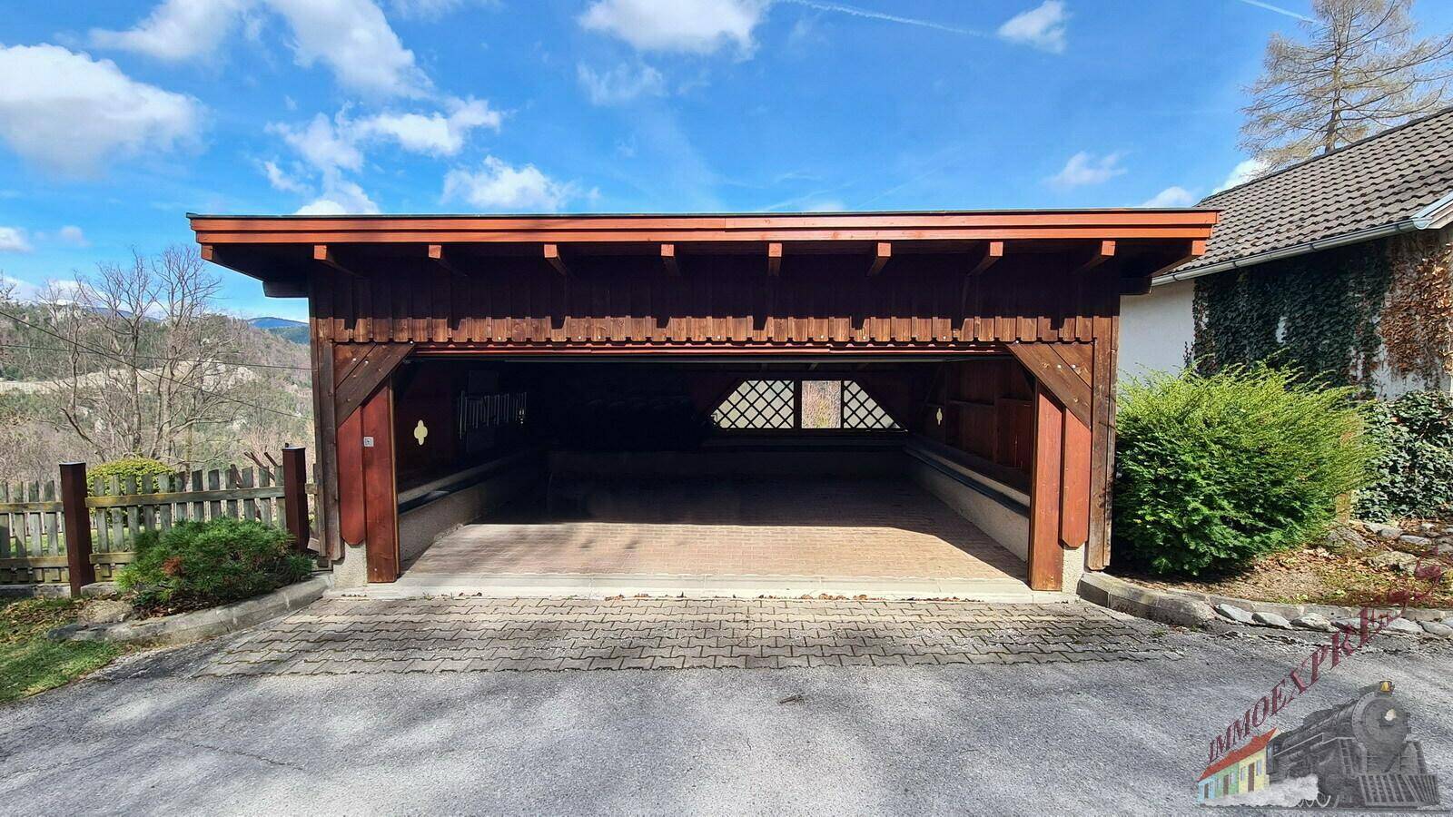Offene Holzgarage mit gepflasterter Zufahrt und Blick auf die umliegende Landschaft.