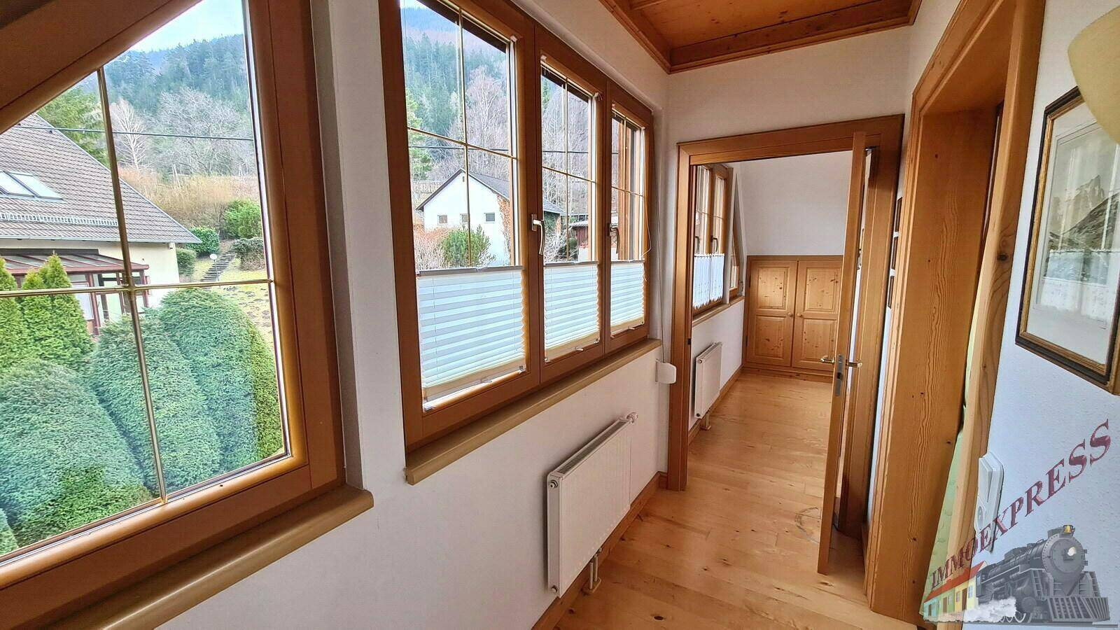 Heller Flur mit Holzboden und großen Fenstern, die viel Tageslicht hereinlassen und Ausblick bieten.