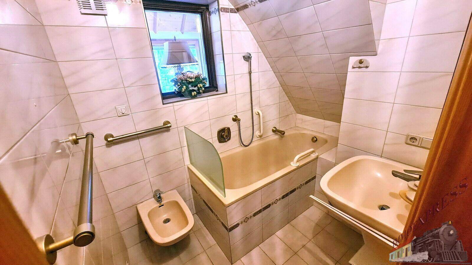 Badezimmer im Dachgeschoss mit Badewanne, Bidet und Waschbecken, hell gefliest und mit Dachfenster.