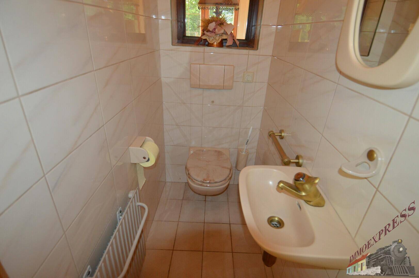 Kleines Gäste-WC mit beigefarbenen Fliesen, Fenster und einfacher Ausstattung.