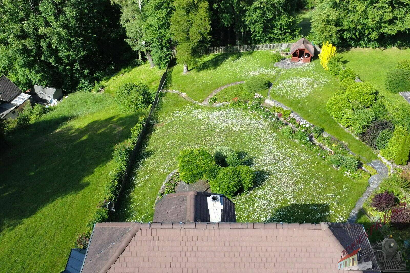 Blick von oben auf den weitläufigen Garten mit Blumenwiese und einem kleinen Gartenhaus.