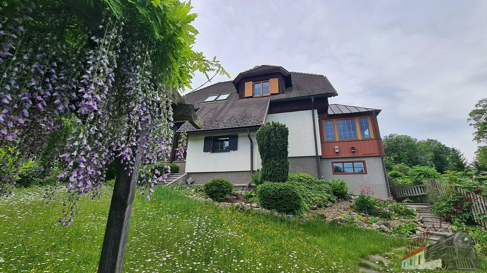 Seitenansicht des Hauses mit blühendem Blauregen und gepflegter Gartenanlage.