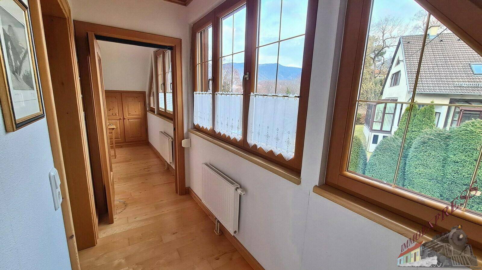 Flur mit Holzboden und Fenstern, die einen Blick auf die umliegende Landschaft ermöglichen.