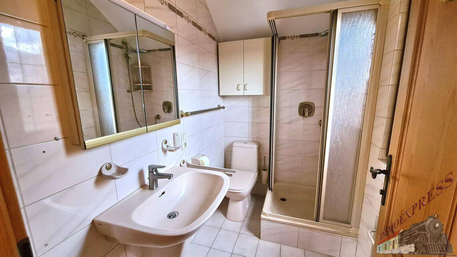 Badezimmer mit Dusche, Waschbecken und WC, hell gefliest und funktional eingerichtet.
