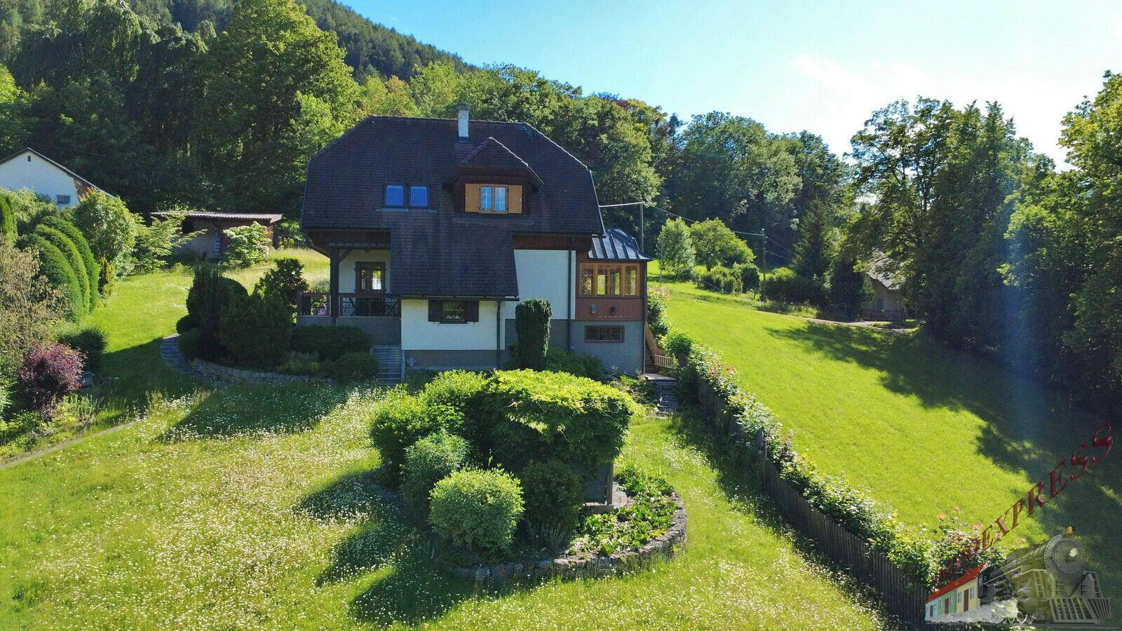 Seitenansicht des Hauses mit gepflegter Gartenanlage und Blick auf die grüne Umgebung.
