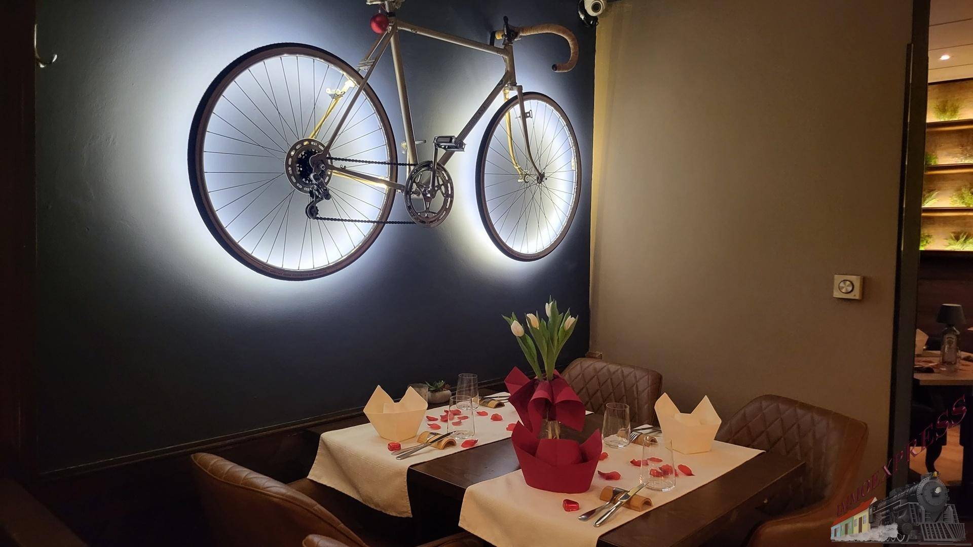Intimer Restauranttisch für zwei Personen, festlich dekoriert, mit einem beleuchteten Fahrrad als Wandkunst.