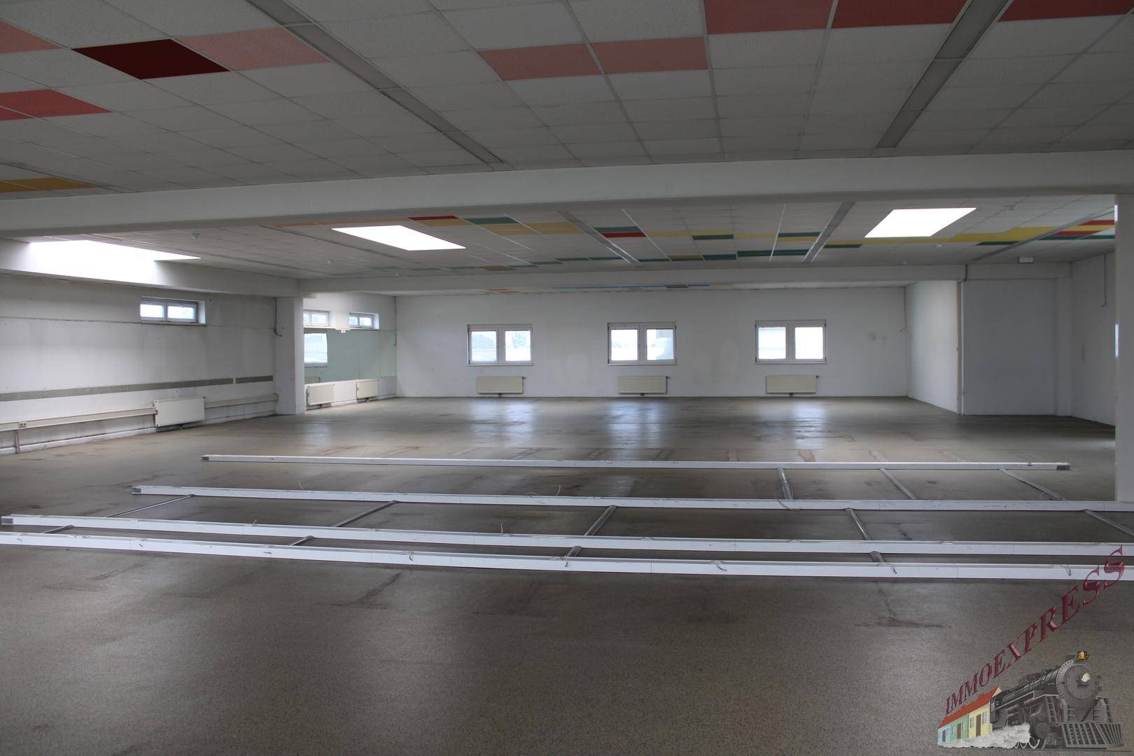 Großer, leerer Büroraum mit vielen Fenstern, Rasterdecke und vorbereiteten Installationen am Boden.