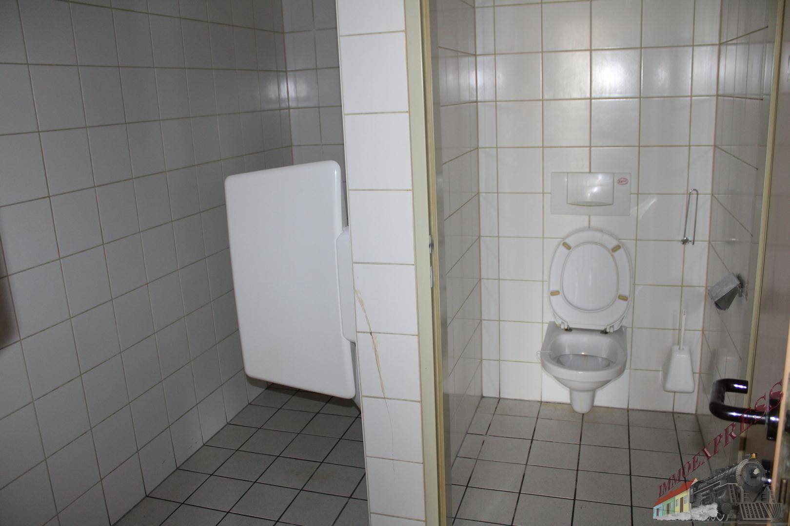 Toilettenraum mit weißen Fliesen, Wand-WC und einem Wickeltisch oder Klappsitz.