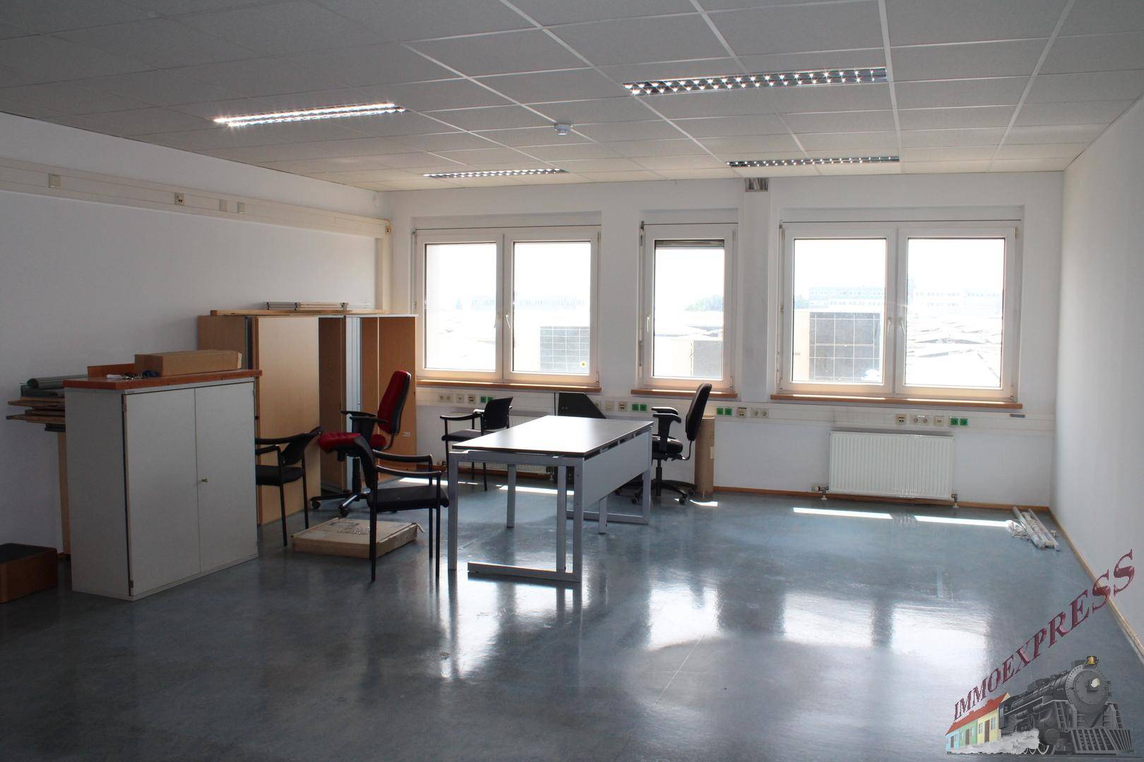 Büroraum mit Schreibtischen, Bürostühlen und Schränken, ausgestattet mit grauem Boden und Rasterdecke.