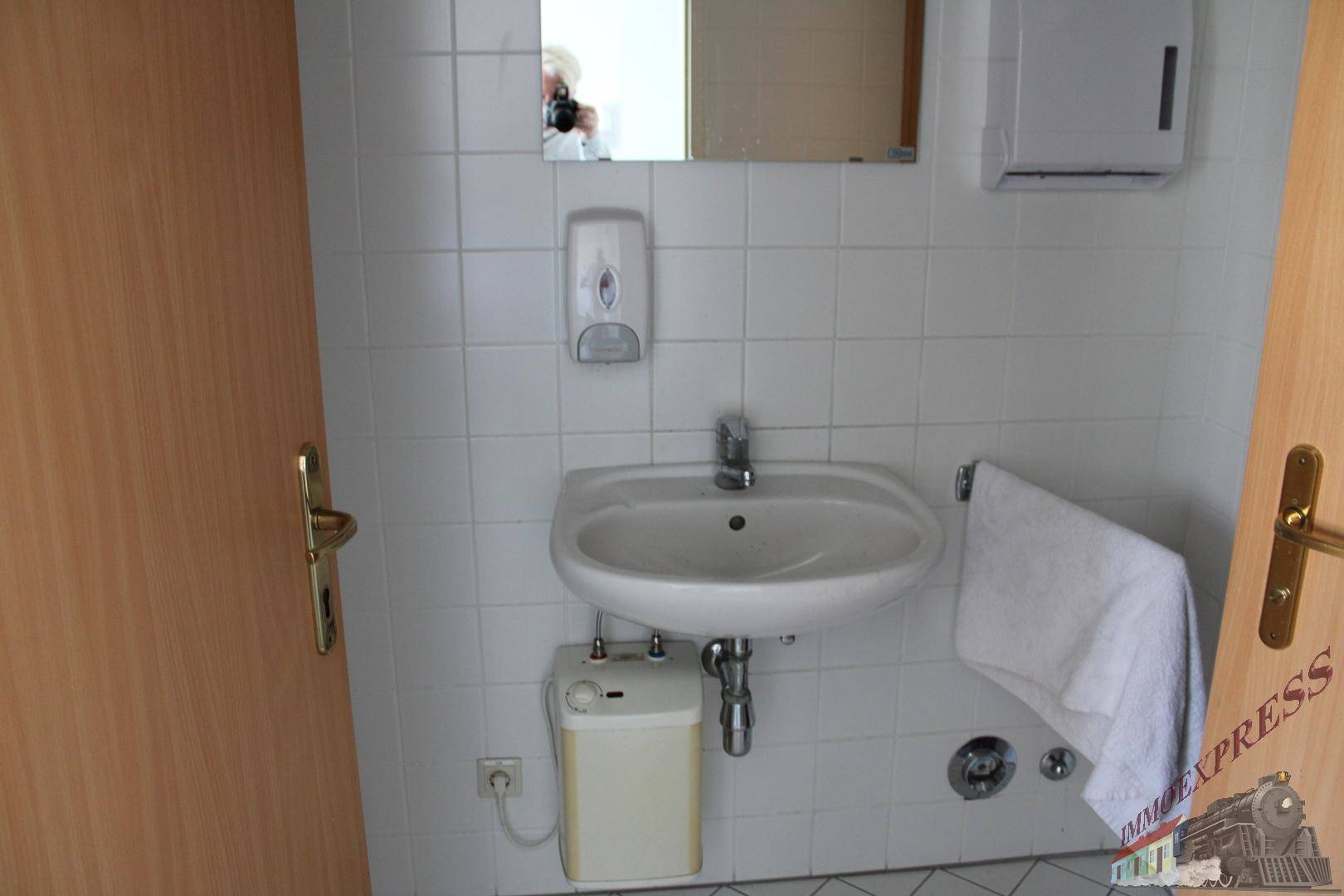 Toilettenraum mit Waschbecken und Spiegel, umgeben von weißen Fliesen und Holztüren.