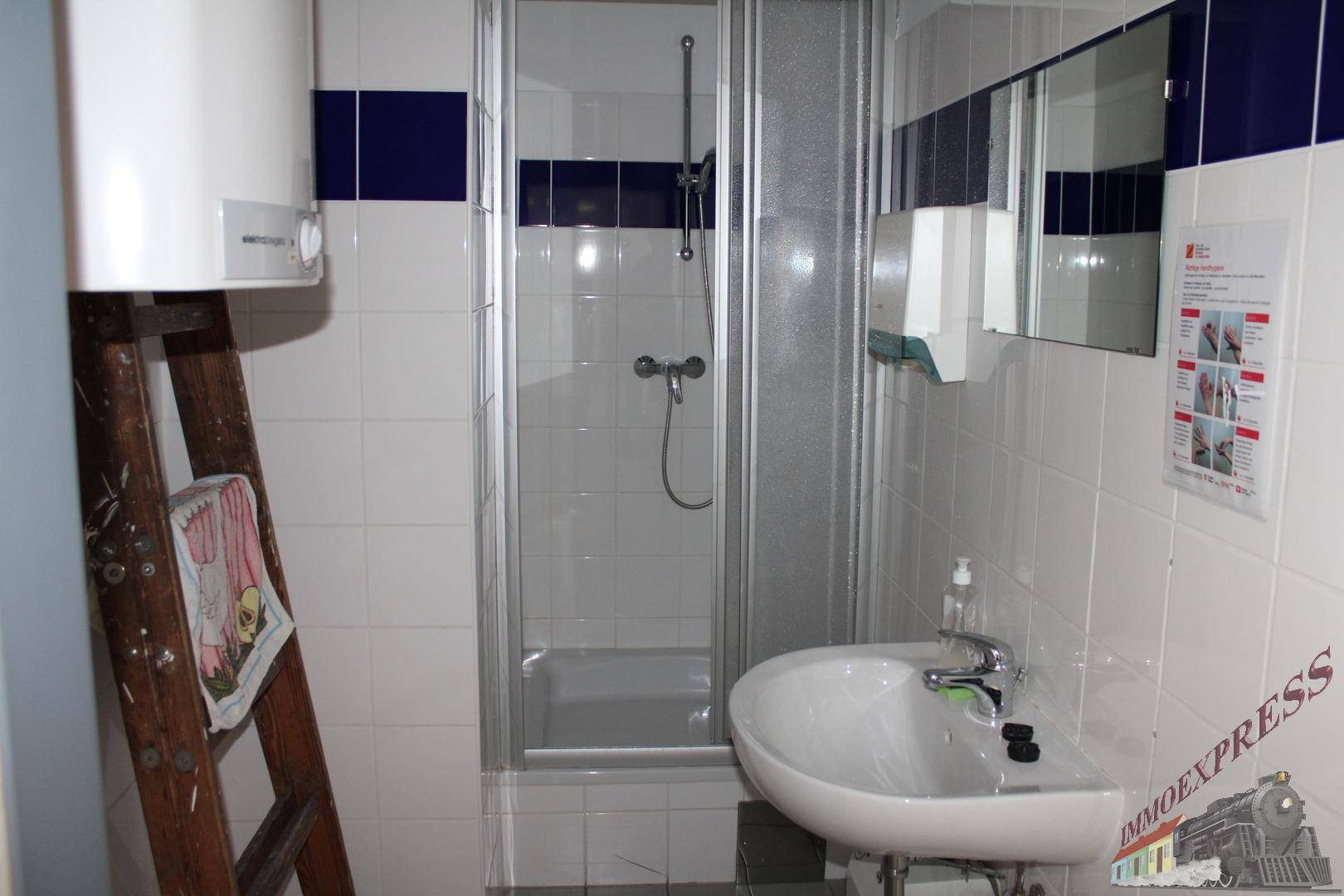 Funktionales Badezimmer mit Duschkabine, Waschbecken und Wandspiegel, gefliest in Weiß mit blauen Akzenten.