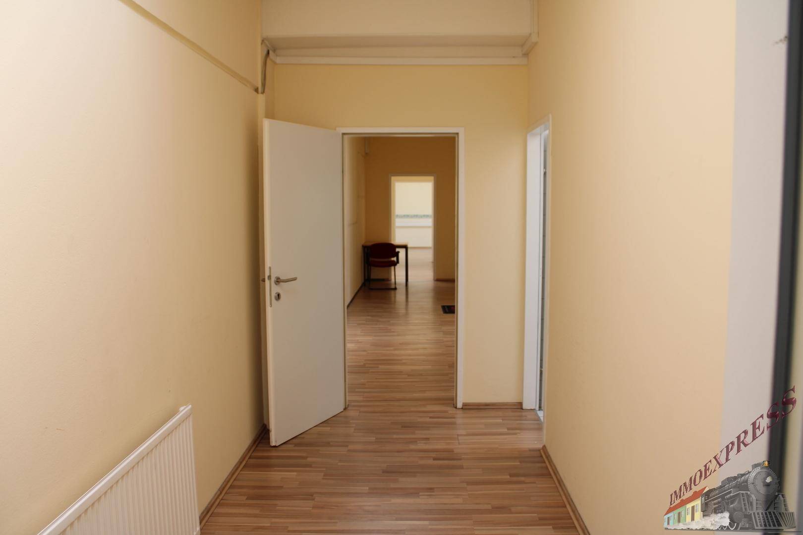 Langer Flur mit Laminatboden, beigen Wänden und offener Tür zu einem weiteren Raum.