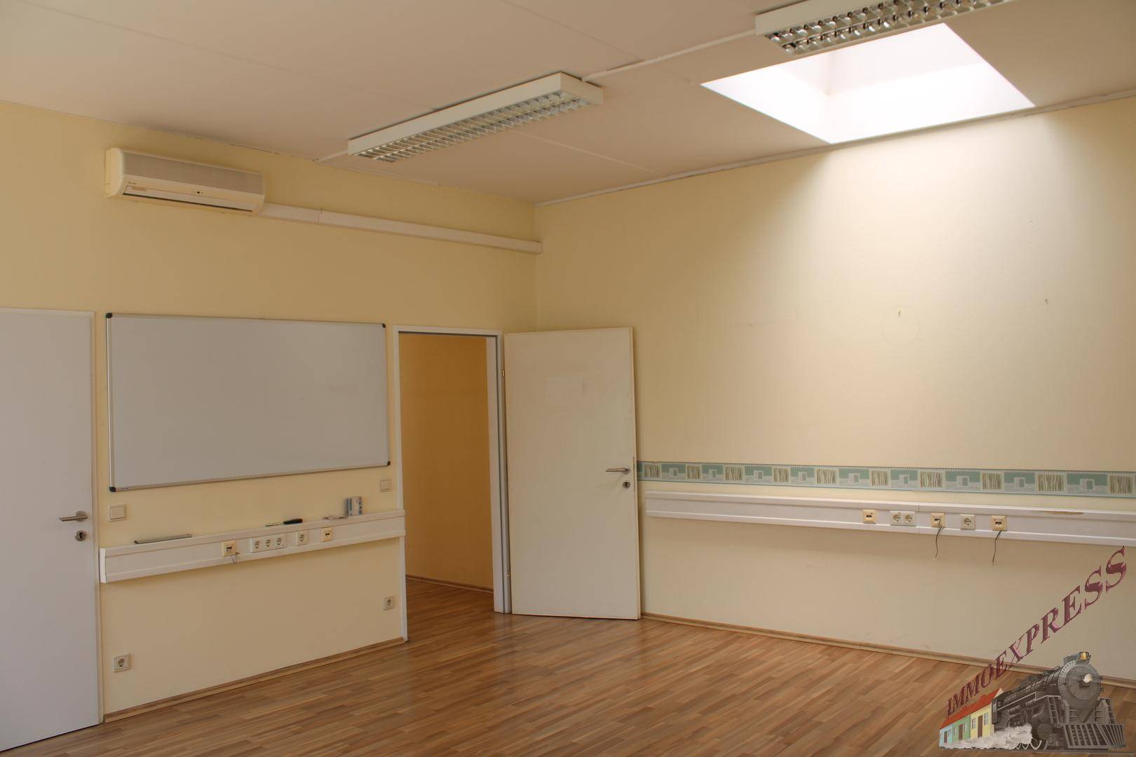 Büroraum mit Laminatboden, Klimaanlage und Whiteboard an der Wand.