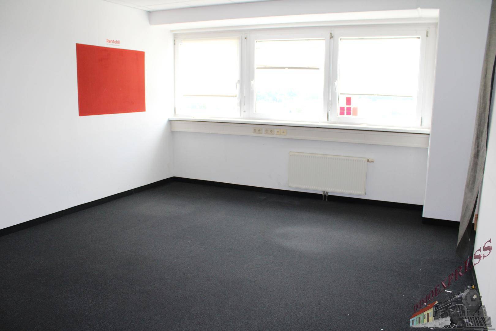 Kleines Büro mit dunklem Teppichboden, weißen Wänden und einem roten Akzentfeld.