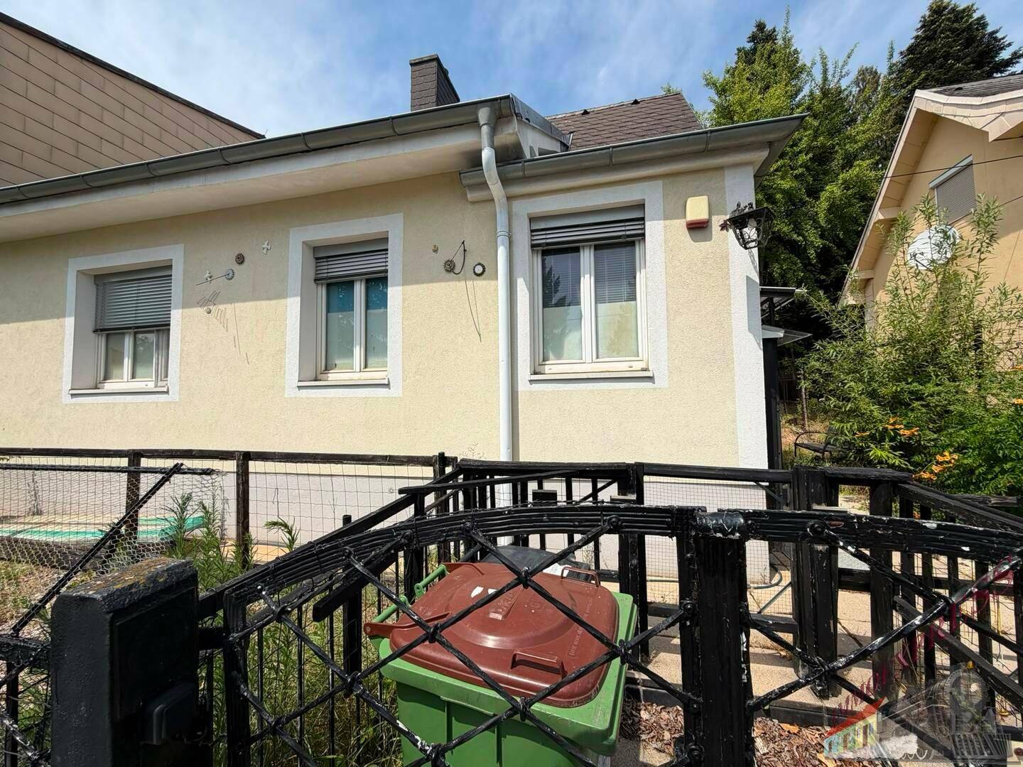 Seitenansicht des Hauses mit Fenstern, Rollläden und einem Zaun im Vordergrund.